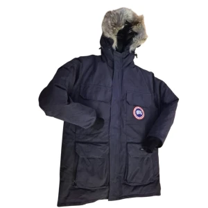 Mörkblå dunparkas från Canada Goose Men  - Säljer en mörkblå parkas från Canada Goose med dunfyllning och stor huva med päls. Jackan har flera praktiska fickor, dragkedja och knäppning framtill samt klassisk logga på bröstet. Perfekt för kalla vinterdagar och riktigt snygg stil.