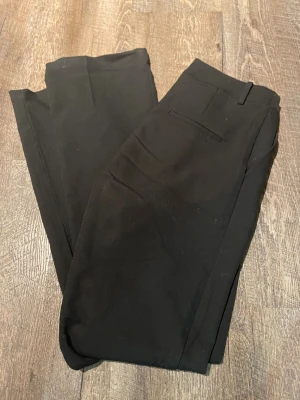 Svarta kostymbyxor från Bik Bok - Snygga svarta kostymbyxor från Bik Bok i klassisk rak modell. Byxorna har diskreta fickor bak och är tillverkade i ett mjukt, välsittande material som ger en clean och stilren look. Perfekta för dig som gillar minimalistisk stil.