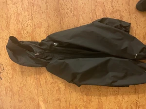 Svart regnjacka från The North Face - Svart regnjacka från The North Face med huva och dragkedja framtill. Jackan har meshfoder på insidan för extra komfort och logga på både bröstet och ryggen. Perfekt för blöta dagar och enkel att slänga på sig när det regnar.