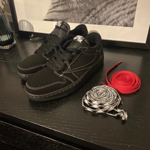 Nike Low Travis Scott  - Svarta Nike Air Jordan 1 Low Travis Scott med kontrasterande vita sömmar och broderad bi på hälen. Skorna har snörning och kommer med extra röda och svartvita skosnören. Jag kan inte ha dom. Dom är helt nya. Hör av er vid frågor 