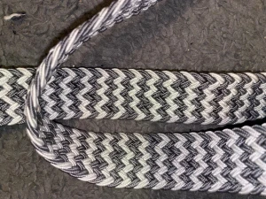 Svartvit zigzag-mönstrat bälte 115cm - Säljer ett svartvitt bälte från J&L med snyggt zigzag-mönster. Bältet är flätat och har detaljer i syntetläder vid spännet. Spännet är svart och metalliskt, vilket ger en cool kontrast till det mönstrade bandet. Materialet är nylon och elastan för extra stretch.