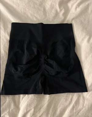 Svarta högmidjade seamless shorts - Säljer ett par svarta högmidjade seamless shorts med tight passform. De har bred resår i midjan och är tillverkade i ett mjukt och stretchigt syntetmaterial som sitter skönt mot kroppen. Perfekta för träning eller chill dagar.💞