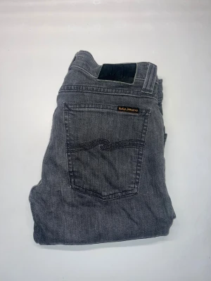 Nudie Jeans - Säljer ett par grå jeans från Nudie Jeans, thigh long John. Modellen har rak passform och är tillverkad i mjuk bomull med lite stretch för extra komfort. Midja 34cm, längd 101cm. Ifall det inte finns någon bild i annonsen där jag bär plaggen jag säljer så är det för att jag ej kan ha storleken heller passformen, så kolla måtten för storlek och googla på modellnamnet för passform 😉 60