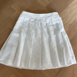 Vit plisserad kjol från H&M Divided - Superfin vit plisserad kjol från H&M Divided i kort modell. Kjolen har bred linning och tydliga veck som ger en snygg och sportig look. Perfekt att styla med sneakers eller boots för en trendig vibe.