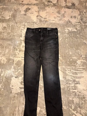 Svarta Replay jeans, straight fit - Säljer ett par svarta Replay Blue Jeans med klassisk femficksdesign och raka ben. Jeansen har snygga detaljer vid bakfickorna och en vit Replay-patch i midjan. Materialet är slitstarkt denim och passformen är straight, perfekt för en chill och stilren look. Helt nya, köptes för 1400kr