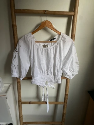 Vit blus med broderade ärmar Gina Tricot - Superfin vit blus från Gina Tricot i storlek S. Blusen har puffiga trekvartsärmar med broderade detaljer och öppna partier, smockad midja och knytband både fram och bak. Perfekt för dig som gillar romantisk och trendig stil.