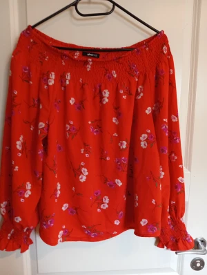 Röd blommig blus från Gina Tricot - Säljer en röd blus från Gina Tricot med blommigt mönster i vitt och lila. Blusen har offshoulder-design, långa ärmar med smock vid ärmslut och halsringning. Luftig och flowy passform, perfekt för att sticka ut med färg och mönster.