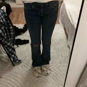 Blå bootcut jeans från Zara - Säljer ett par mörkblå jeans från Zara i bootcut-modell med slitning vid knät. Klassisk femficksdesign och gul kontrastsöm. Jeansen har normal passform och är tillverkade i jeansmaterial. Perfekt för dig som gillar retrovibbar och snygg siluett.