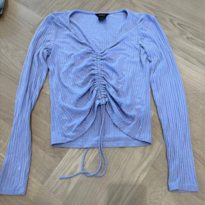 Ljuslila ribbad topp från Lindex - Säljer en ljuslila långärmad topp från Lindex i ribbad bomull. Toppen har v-ringning och snygg snörning framtill som ger en ruched effekt. Croppad passform och mjukt material som sitter skönt. Perfekt för dig som gillar trendiga detaljer och pastellfärger.