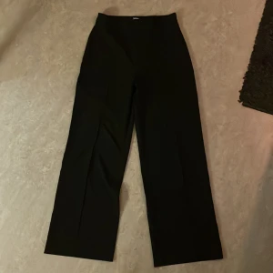 Svarta wide kostymbyxor Pull&Bear - Snygga svarta kostymbyxor från Pull&Bear i storlek L. Byxorna har en hög midja och ett wide ben som ger en modern och avslappnad siluett. Perfekta för dig som gillar stilrena och trendiga plagg. Materialet känns mjukt och följsamt.