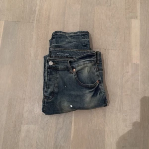 Purple Brand jeans med färgstänk - Snygga jeans från Purple Brand i mörkblå tvätt med coola färgstänk i vitt och rött. Modellen har klassisk femficksdesign, raka ben och slitningar för en edgy vibe. Jeansen är tillverkade i robust denim och har detaljerade sömmar och knappstängning.