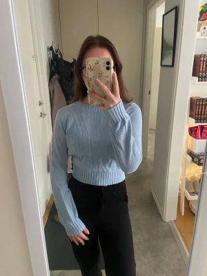 Ljusblå cropped stickad tröja - Säljer en ljusblå cropped stickad tröja med rund halsringning och bred ribbad mudd vid midjan och ärmsluten. Tröjan har en enkel och clean design som passar perfekt till höstens och vinterns outfits.