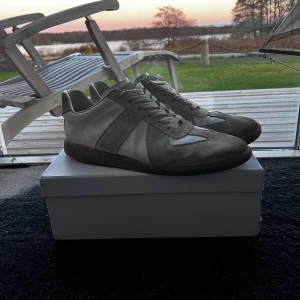 Maison Margiela Replica sneakers beige - Maison Margiela Replica sneakers i beige och vitt med klassisk retrodesign. Ovandel i mocka och skinn, bruna gummisulor och snörning. Skick 8/10, någon missfärgning som säkert gå bort med en tvätt. Storlek 44, allt og följer med men kvitto saknas. Äktahetsbevis saknas därav priset. Pris går att diskutera✅