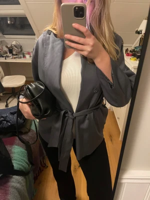 Trenchcoat från Carin Wester - Snygg grå/blå trenchcoat från Carin Wester med knytbälte i midjan och knappar framtill. Jackan har en rak och loose passform