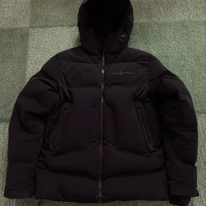 Svart Sail Racing pufferjacka med huva - Svart Sail Racing Drift jacket i storlek S, använt men fint skick. Nypris ligger på 6000kr. Mitt pris 1200. Jackan har några slitningar (märket på bröstet och inuti) och en liten defekt på dragkedjan som inte märks så mycket. Jackan är väldigt varm och passar perfekt för en kall svensk vinter🙌🏽 Hör av er vid frågor