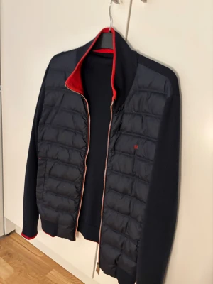  Carolina Herrera cardigan -  från Carolina Herrera med quiltad front och stickade ärmar. Röd insida på kragen och detaljer vid dragkedjan. Tvåvägsdragkedja med CH-logga, innerficka med röd kant och broderad logga på bröstet. Perfekt för dig som gillar stilrena och sportiga jackor. Nypris cirka 4000