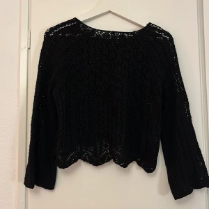 Svart spetsblus med lång ärm - Säljer en svart blus med lång ärm i spets och broderad design. Blusen har en vågig nederkant och är genombruten med snygga detaljer. Perfekt för dig som gillar en elegant och cool stil.