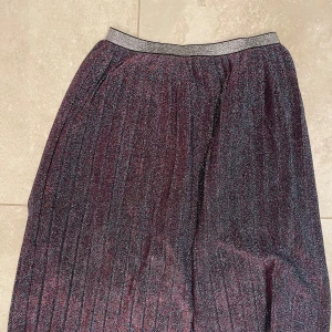 Glittrig plisserad kjol från Name It - Glittrig plisserad långkjol från Name It. Skimrande och festlig.  Resår i midjan. 