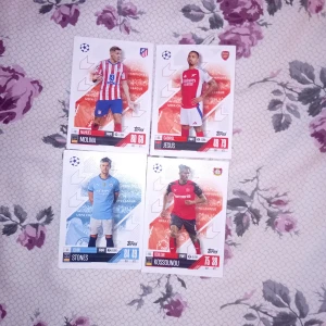 Match Attax UEFA Champions League Trading Cards - Samling med fyra Match Attax UEFA Champions League trading cards med spelare från Atlético Madrid, Arsenal, Manchester City och Bayer Leverkusen. Perfekt för unga fotbollsfans och samlare som vill ha coola kort med sina favoritspelare och lag.