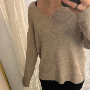 Beige ribbad stickad tröja - Mysig beige stickad tröja med ribbad struktur och v-ringad hals. Tröjan har en loose passform och långa ärmar, perfekt för att hålla sig varm under kyliga dagar. Enkel och stilren design som är lätt att matcha med olika outfits.