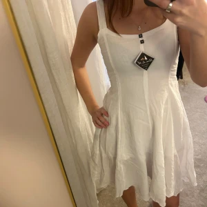 Vit kortklänning från Positano - Supersöt vit klänning från Positano, köpt i Italien, med skön passform och ärmlös design. Klänningen har en lätt utställd kjol och breda axelband, perfekt för sommarens varma dagar. Tillverkad i luftigt linne som ger en fräsch och avslappnad vibe.