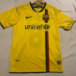 Gul FC Barcelona Iniesta tröja Nike S 2008/09  - Säljer en gul FC Barcelona fotbollströja med Iniesta och nummer 8 på ryggen. Tröjan har svarta detaljer, klubbmärke på bröstet, UNICEF-logga och en vertikal röd-grön rand. Tillverkad i lätt polyester med NikeFIT-teknologi och svart krage.