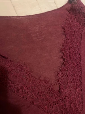 Vinröd långärmad blus med spets (S) - Säljer en vinröd långärmad blus från Intimissimi med v-ringad hals och dekorativ spets både vid halsringningen och ärmsluten. Tunn och mjuk i materialet, perfekt för dig som gillar romantiska detaljer och snygg passform.