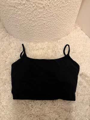 Svart träningstopp från shein - Svart träningstopp med smala axelband från shein. Toppen har en enkel och stilren design med en croppad passform och ett litet G-tryck på framsidan. 