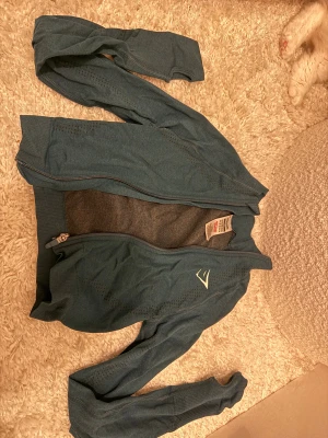 Mörk grön träningsjacka från Gymshark XS - Säljer en mörk grön långärmad träningsjacka från Gymshark i storlek XS. Jackan har dragkedja framtill, diskreta ventilationshål längs ärmarna och en sportig look med Gymshark-logga på bröstet. 