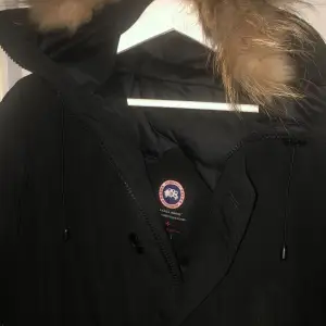 Säljer en svart vinterjacka från Canada Goose med pälsdetaljer på huvan. Jackan är perfekt för kalla vinterdagar och har en klassisk design med lång ärm och dragkedja fast den e sönder därför säljer jag den billigare. Den är i mycket bra skick och håller dig varm och stilren hela säsongen. Kostade 19.990kr ny säljer för 3000kr