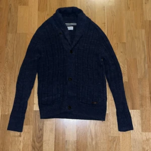 Mörkblå kofta från Pier One - Säljer en snygg mörkblå kofta från Pier One. Den är stickad med ett ribbat mönster och har stora knappar framtill. Perfekt för höst och vinter, med långa ärmar och en mysig krage. Passar både till vardags och lite finare tillfällen. Endast använd 1-2 gånger - kom med prisförslag 