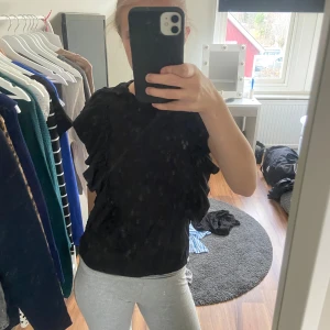 Svart topp med volanger - Säljer en snygg svart topp med volanger längs sidorna. Perfekt för en kväll ute eller en fest. Toppen är i ett mjukt material och har en normal passform. Den är kortärmad och ger en stilren look. Passar bra till både jeans och kjol! Pris kan diskuteras 💕💕