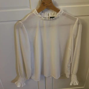 Blus från Gina Tricot - Tunn vit blus från Gina Tricot i storlek 40. Söt krås i halsen och i ärmslut. Använd men har mycket kvar att ge. 