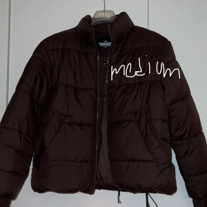Brun pufferjacka - Säljer en brun pufferjacka i storlek medium. Den är perfekt för kyliga dagar med sin vadderade design och dragkedja framtill. Jackan har långa ärmar och en hög krage för extra värme. Passar både till vardags och lite mer avslappnade tillfällen.