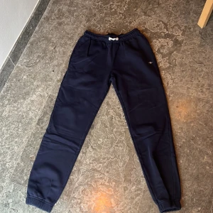 Mörkblå mjukisbyxor från GANT - Säljer ett par mörkblå mjukisbyxor från GANT i mycket bra skick. De är superbekväma med elastisk midja och snörning. Perfekta för en chill dag hemma eller en snabb tur till affären. Liten i storleken. 
