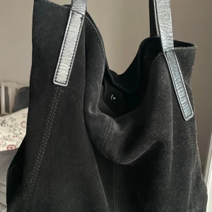 Svart axelväska från Anna Field - Snygg svart axelväska från Anna Field i mocka med stilrena detaljer. Perfekt för både vardag och fest. Väskan har en enkel design med två långa axelremmar och en rymlig insida. Den är i bra skick med lite slitage på remmarna. En klassisk och tidlös väska som passar till allt! Lite slitage på handtagen