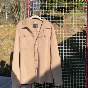 Säljer en snygg beige overshirt från Pelle P i mycket bra skick. Den har långa ärmar och knappar framtill. Perfekt för höst och vår, och funkar både som jacka och skjorta. Storlek herr M. 