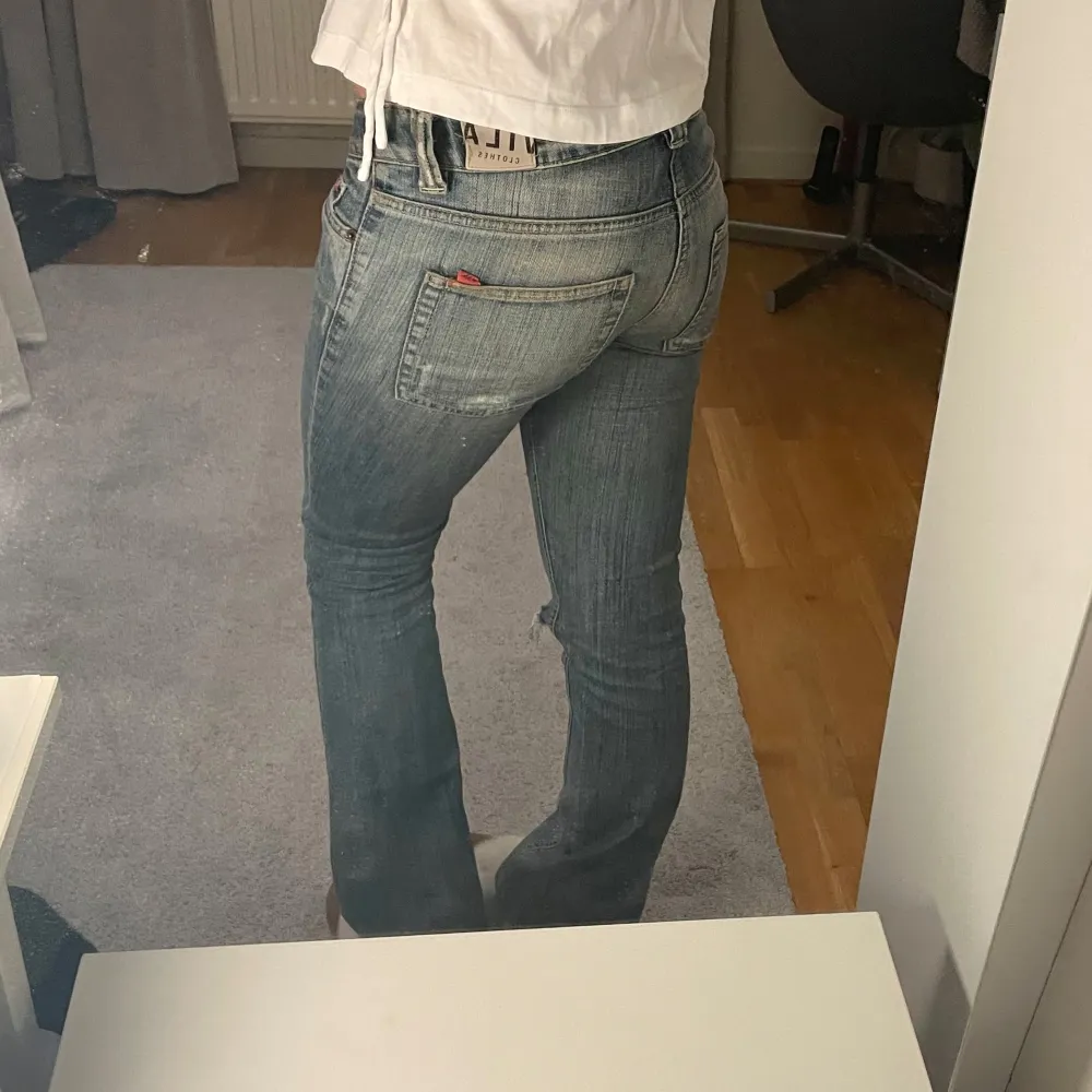 Säljer ett par snygga blå jeans med slitningar på knäet. De är lågmidjade och har en bootcut-stil som ger en retro vibe. Perfekta för en avslappnad look. Passar bra till både vardag och fest!. Jeans & Byxor.