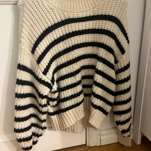 Randig stickad tröja i beige och svart - Mysig och oversized stickad tröja i beige med svarta ränder. Perfekt för höst och vinter, med långa ärmar och en avslappnad passform. Den är superbekväm och passar till både jeans och kjol. Ett måste för garderoben!