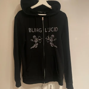 Rhinestone hoodie - Snygg svart hoodie från Bling Lucid , Tröjan har en dragkedja och en luva, perfekt för en cool och avslappnad stil. Den har långa ärmar och är gjord i ett mjukt material.