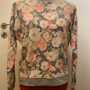 Blommig tröja med långa ärmar MNG M - Säljer en mysig tröja med ett vackert blommönster i rosa, beige och grå toner. Tröjan har långa ärmar och en rund halsringning. Perfekt för en avslappnad stil.  MNG collection Armhåla till armhåla: 45 cm Bortklippta tvättråd  Inga bilder när den sitter på mig! Katter finns i hemmet