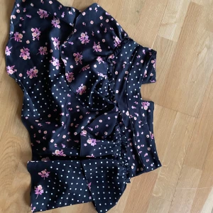 Blommig och prickig kjol från For Love & Lemons - Snygg kjol med en mix av blommigt och prickigt mönster i rosa och vitt på en mörkblå bakgrund. Kjolen har volangdetaljer och en omlott-design som ger en feminin touch. Perfekt för att sticka ut med en unik stil.