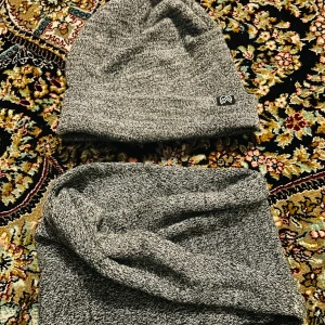 Grå stickad mössa och halsduk från H&M - Snygg och enkel grå stickad mössa och halsduk från H&M. Perfekt för kyliga dagar med en stilren design och diskret logga. Passar både till vardags och mer avslappnade tillfällen.