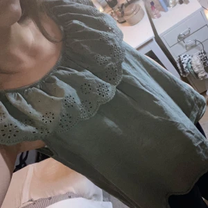 Grön offshoulder topp med spetsdetaljer - Säljer en söt grön offshoulder topp med vackra spetsdetaljer runt halsringningen. Toppen har en luftig passform och är tillverkad i ett mjukt material.