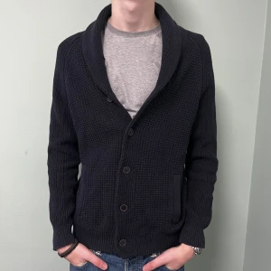 Svart stickad kofta med knappar - Snygg svart stickad kofta med knappar framtill och två fickor. Storlek L, modellen är 195. Hör av er vid intresse.