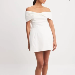 Vit offshoulder klänning - Elegant vit offshoulder klänning med en stilren rosettdetalj framtill. Klänningen har en kort längd. Köpte den för 799 och har aldrig andvänt den. Tanken var ha den till studenten men har hittat en annan klänning🩷 skriv om fler bilder 