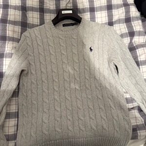 Grå stickad tröja från Ralph Lauren - Säljer en stilren grå stickad tröja från Ralph Lauren med kabelstickat mönster. Tröjan har långa ärmar och en klassisk rund halsring. Perfekt för exempelvis ett par jeans, pris kan diskuteras och va inte rädd att höra av dig vid funderingar!🤩