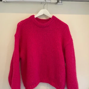 Rosa stickad tröja från Vero Moda - Säljer en härligt rosa stickad tröja från Vero Moda. Tröjan har en klassisk rund hals och långa ärmar, perfekt för kyligare dagar. Den är mjuk och bekväm, idealisk för att hålla sig varm och stilren.