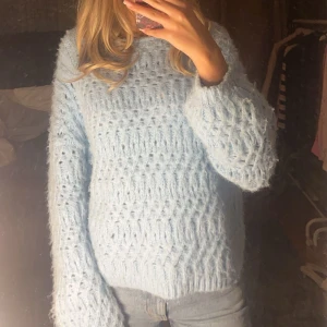 Ljusblå stickad tröja från Vero Moda - Mysig ljusblå stickad tröja från Vero Moda. Perfekt för kyliga dagar med sin fluffiga och varma design. Tröjan har långa ärmar och en bekväm passform.