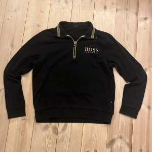 Svart tröja med dragkedja från Hugo Boss - Snygg svart tröja från Hugo Boss med dragkedja och logotyp på bröstet. Tröjan har långa ärmar och en stilren design, perfekt för en avslappnad men ändå elegant look. Passar Xs-S. Är öppen för bud. 